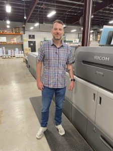 New employee Tom Gross standing next to our Ricoh 9210 with Plockmatic bookletmaker finishing unit.