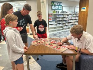 Football player Hunter Wohler at the Muskego Public Library signing READ ON posters.