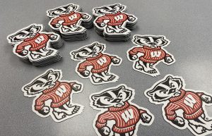 Die-cut Bucky Badger magnets in a stack on a desktop.