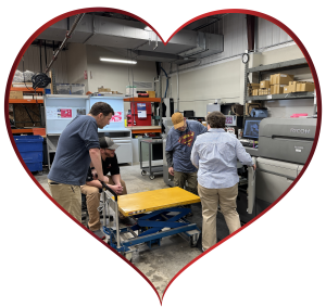 A heart shaped photo of three staff members training with a vendor rep on the Ricoh 9500 high-speed printer.
